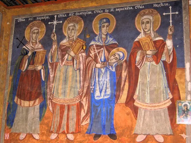 Fresco of four women saints standing side by side with halos and crosses, wearing red, white and blue robes, under a row of Slavonic inscriptions