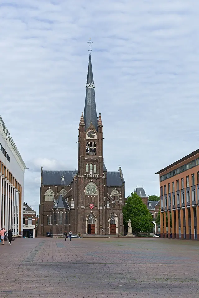 A tall neo-Gothic brick church with a single slender spire rising above a wide paved square in Schiedam