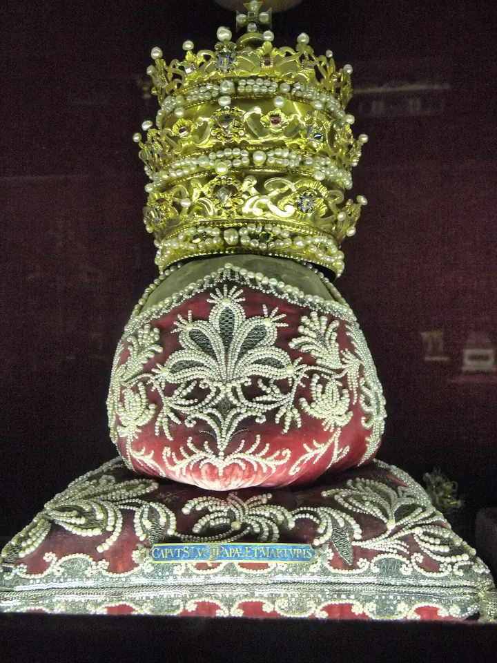 Relic wrapped in red and gold embroidered silk, set on an embroidered cushion and crowned with a jeweled golden papal tiara