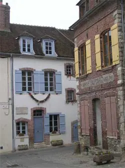 Two old town houses on a narrow street corner in Joigny, one cream with blue shutters and one of red brick with yellow shutters