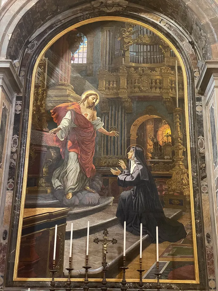 Large mosaic in an arched frame of Christ in a red cloak appearing to a kneeling nun in a black habit inside a church, above an altar with six candles