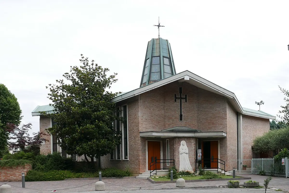 Modern brick church with a tall glass lantern tower topped by a star and a white statue by the entrance, framed by trees