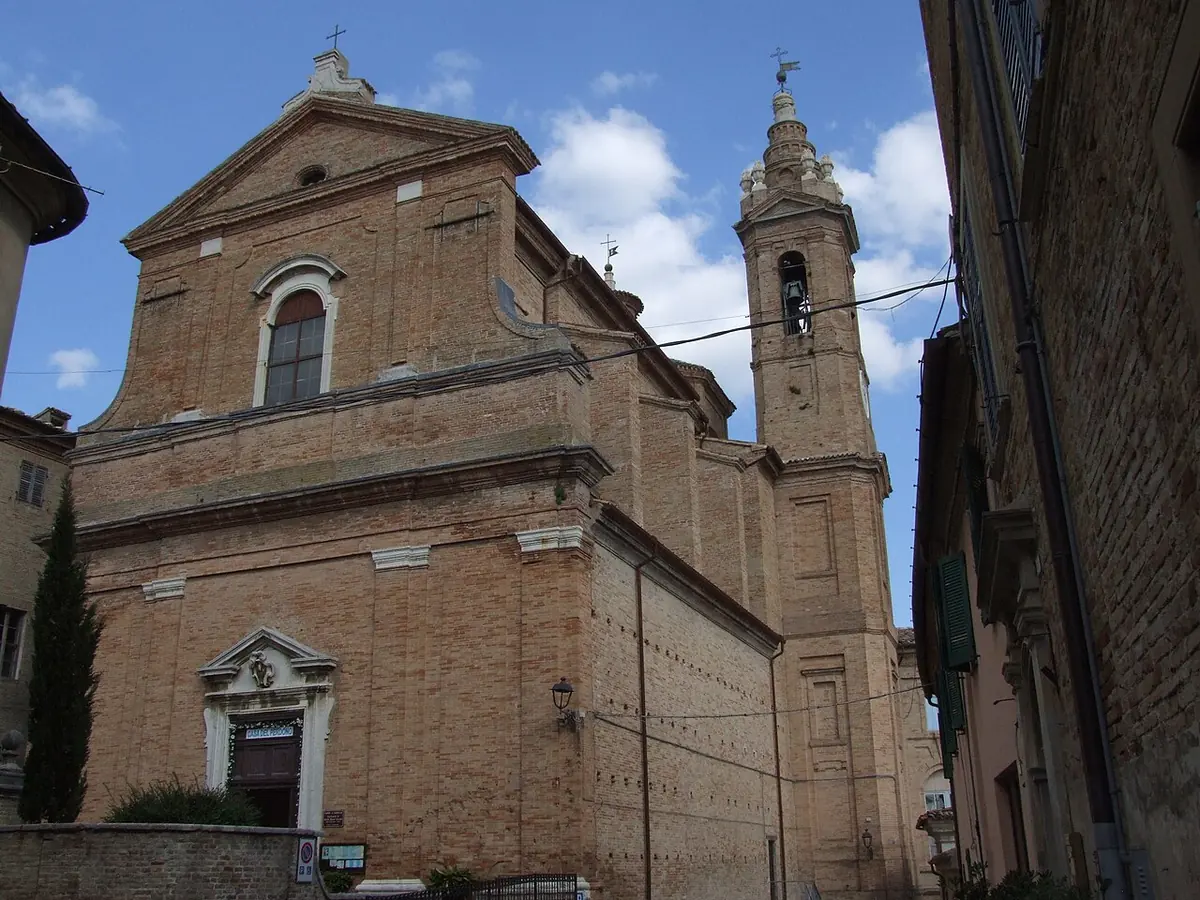 Brick church with a pedimented facade and a bell tower on a narrow street in the hill town of Corinaldo