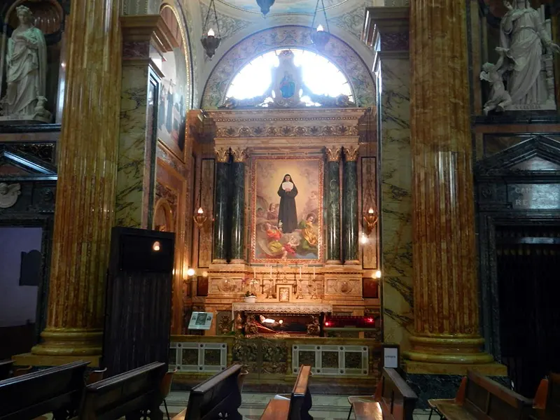 A side chapel framed by marble columns, with an altarpiece of a sister in black above a glass urn in the altar