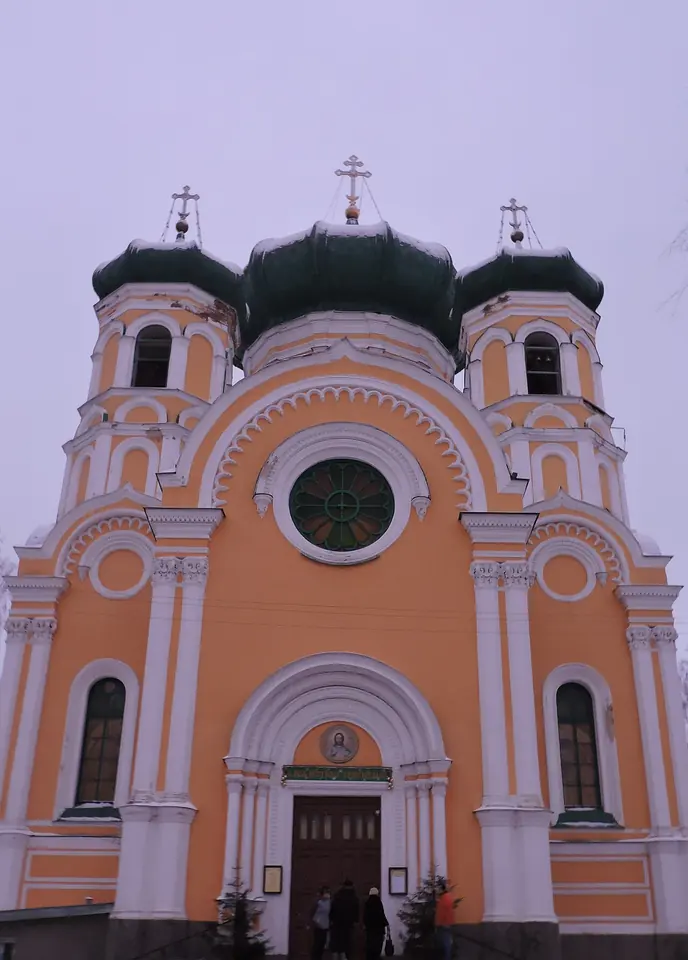 Peach-colored cathedral front with white columns, a round window and dark green domes with gold crosses, in Gatchina, Russia