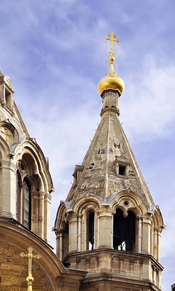 A golden onion dome topped with an Orthodox cross on a pale stone tower of a Russian cathedral against a blue sky