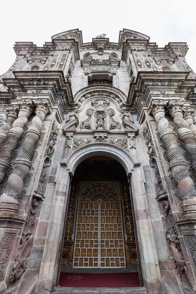 Looking up at the richly carved stone Baroque façade of La Compañía church in Quito, with twisted columns around a tall arched doorway
