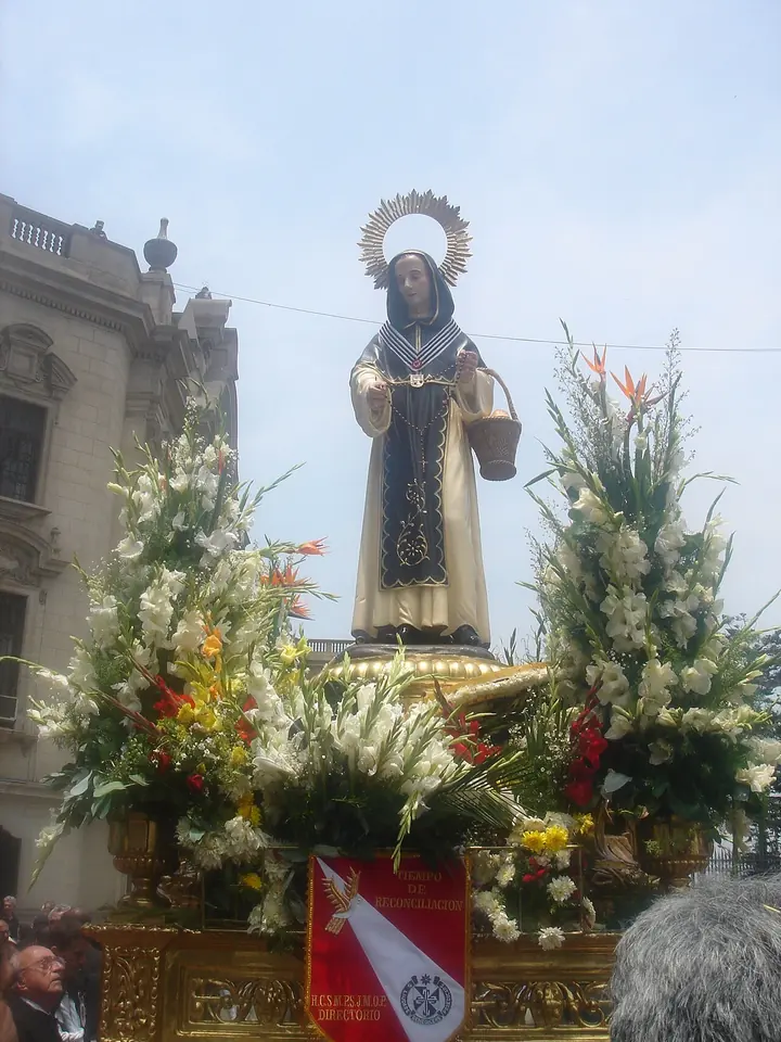 Statue of St. John Macías in a Dominican habit with a halo, carried on a flower-covered platform through a street in Lima
