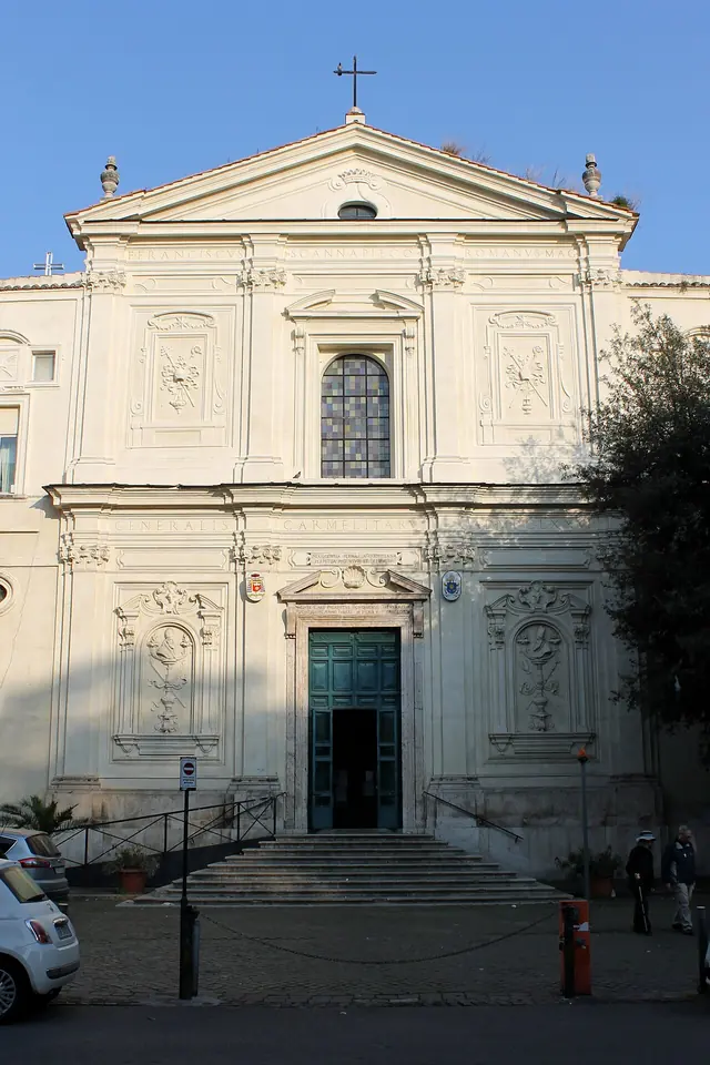 The pale stone facade of a Roman church with a triangular pediment, pilasters and a wide stairway leading up to the door
