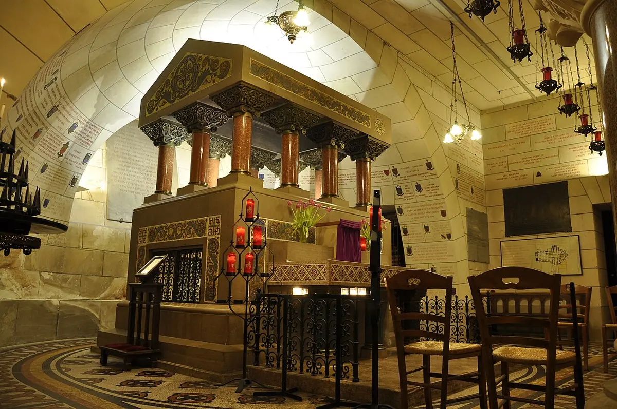 The stone tomb of St. Martin under a canopy on columns in the vaulted crypt of the basilica in Tours, with hanging votive lamps and red candles