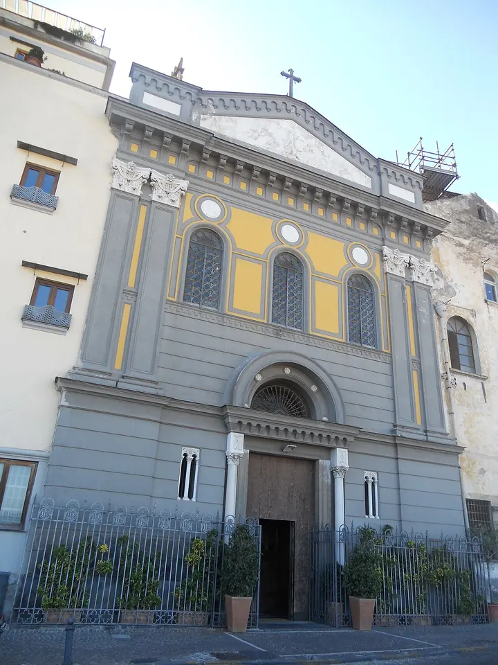 The gray and yellow facade of the church of Santa Lucia al Monte in Naples behind an iron railing