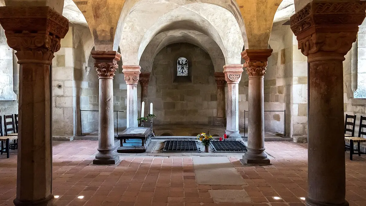 Romanesque crypt with short columns and carved capitals, round arches and stone tombs set in the floor