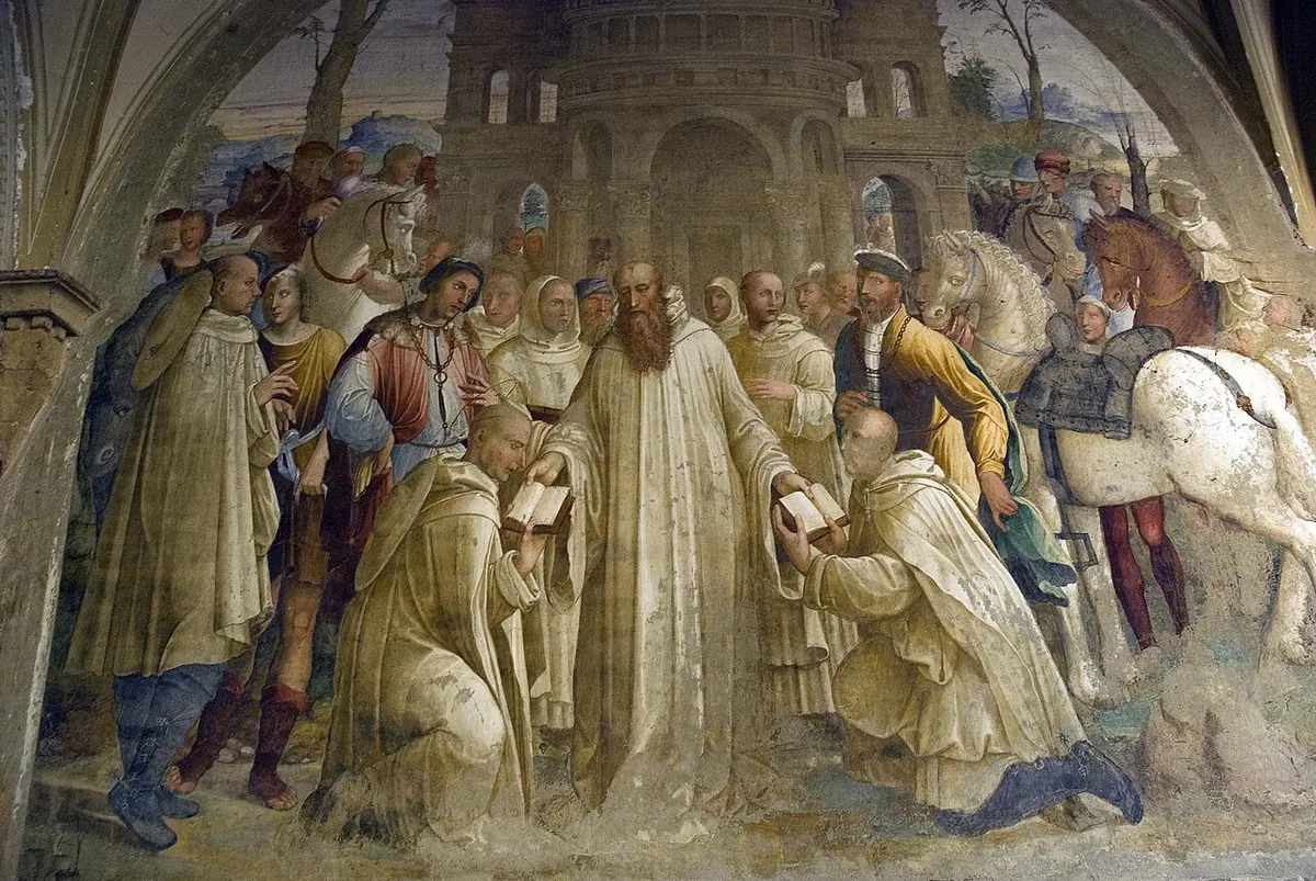 Fresco of St. Benedict in white handing a book to a kneeling monk among a crowd of monks, horsemen and travelers outside a city