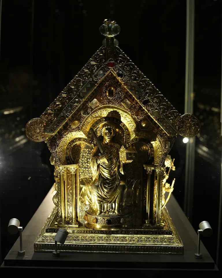 The gilded silver end of a house-shaped Romanesque reliquary, with a seated figure of a saint under an arch, set with gems and filigree