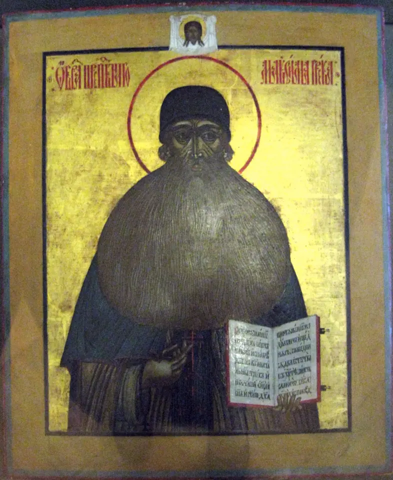 Russian icon on a gold ground of St. Maximus in a dark cowl with a very long beard, holding an open book, with the Holy Face at the top