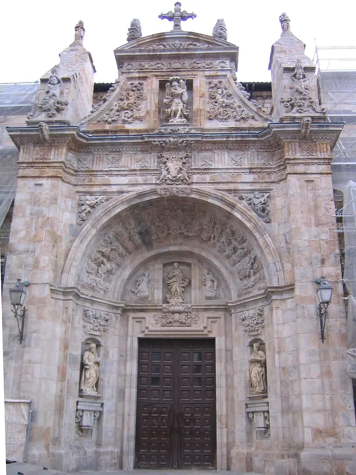 The richly carved Renaissance stone portal of a church, with an arched doorway, statues of saints in niches and an ornate crest crowned by a cross