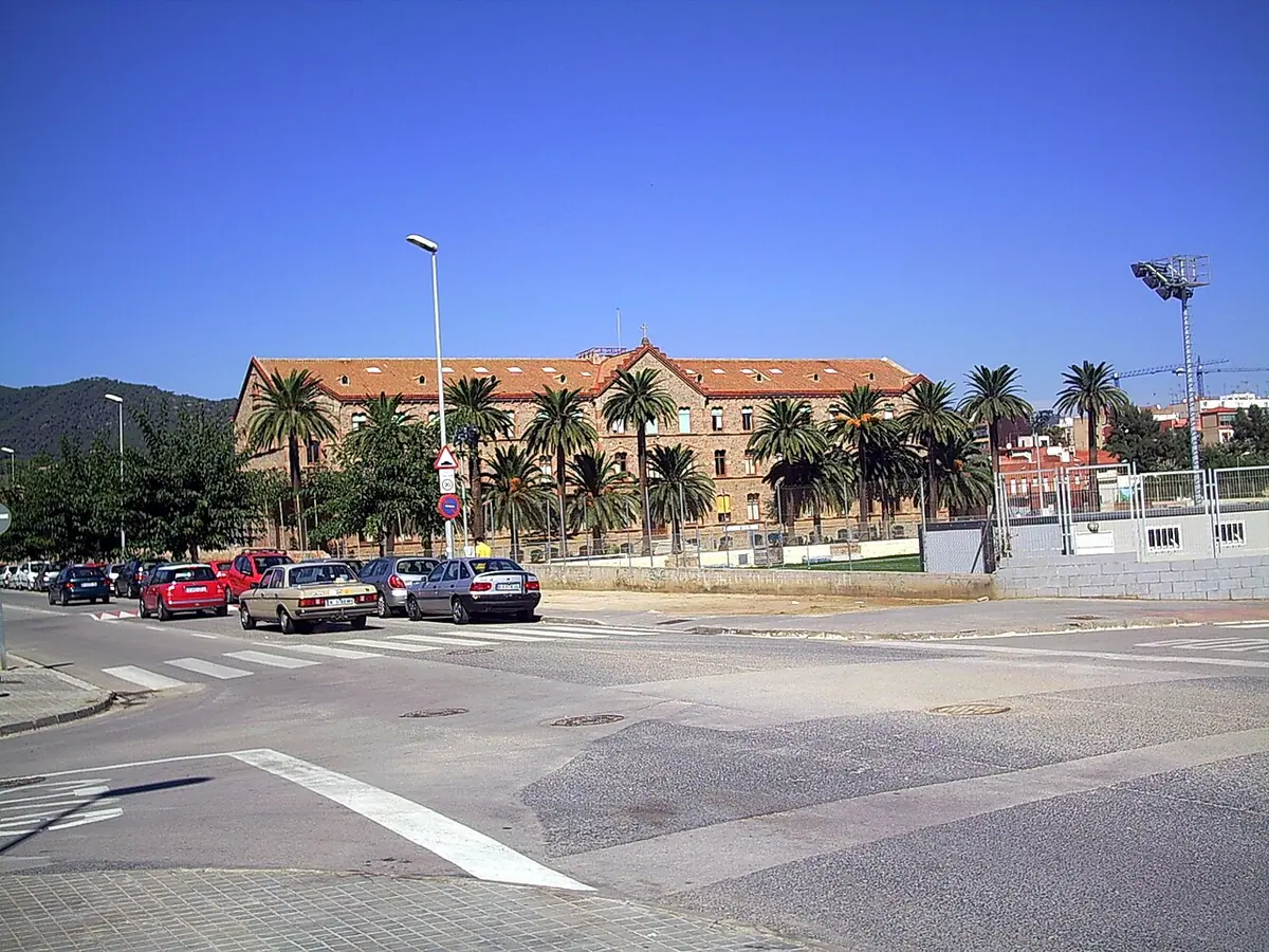 Long three-story building with a red tile roof behind a row of palm trees on the Catalan coast, the La Salle house at Premià de Mar