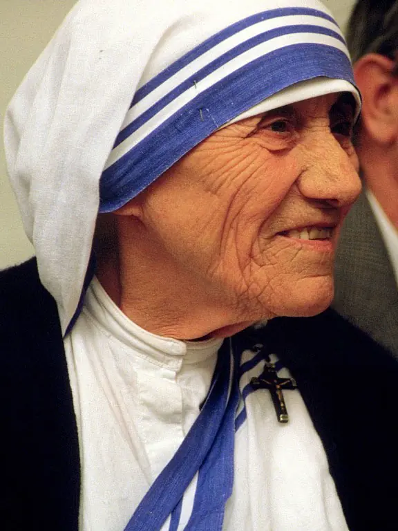 Close color photograph of a smiling Mother Teresa in her white and blue sari, with a small crucifix pinned at her shoulder