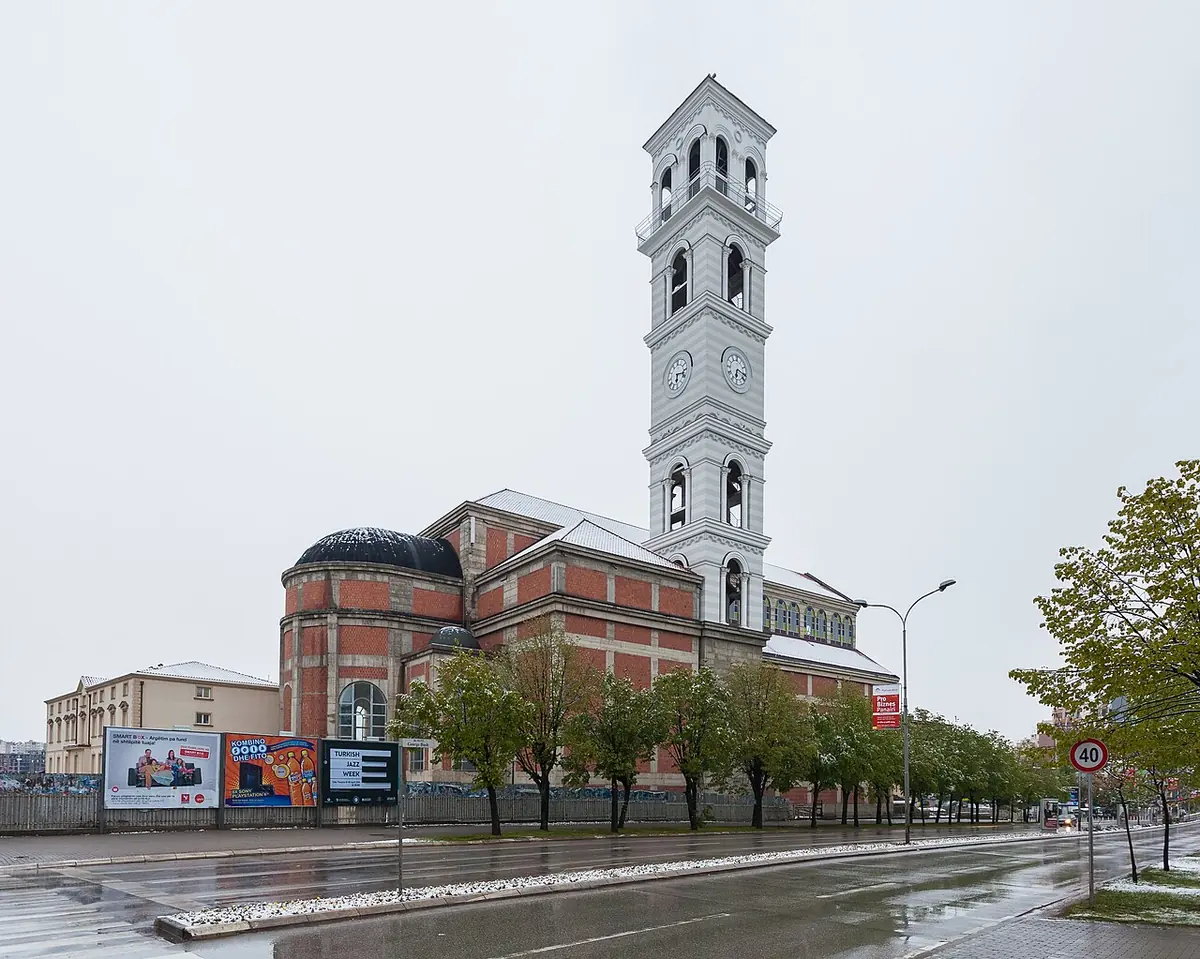 Large red-brick cathedral with a tall white bell tower beside a wide, rain-wet avenue