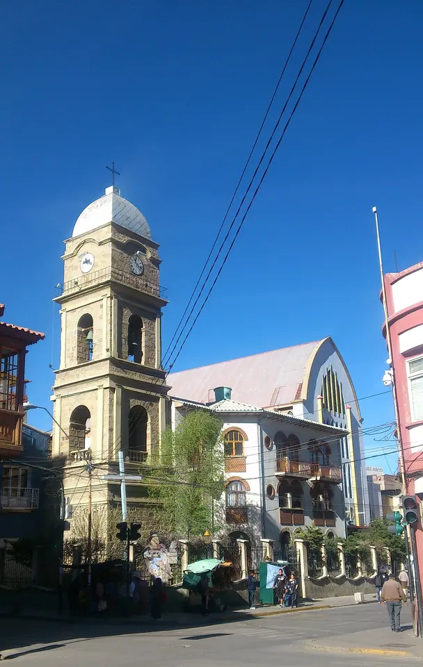 Tall stone bell tower with a white dome beside a church with a pointed gabled roof, on a sunny street corner under a deep blue sky
