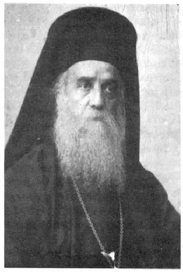 Black-and-white photograph of an elderly bishop with a long white beard in a black monastic veil and cassock, with a small cross on a chain