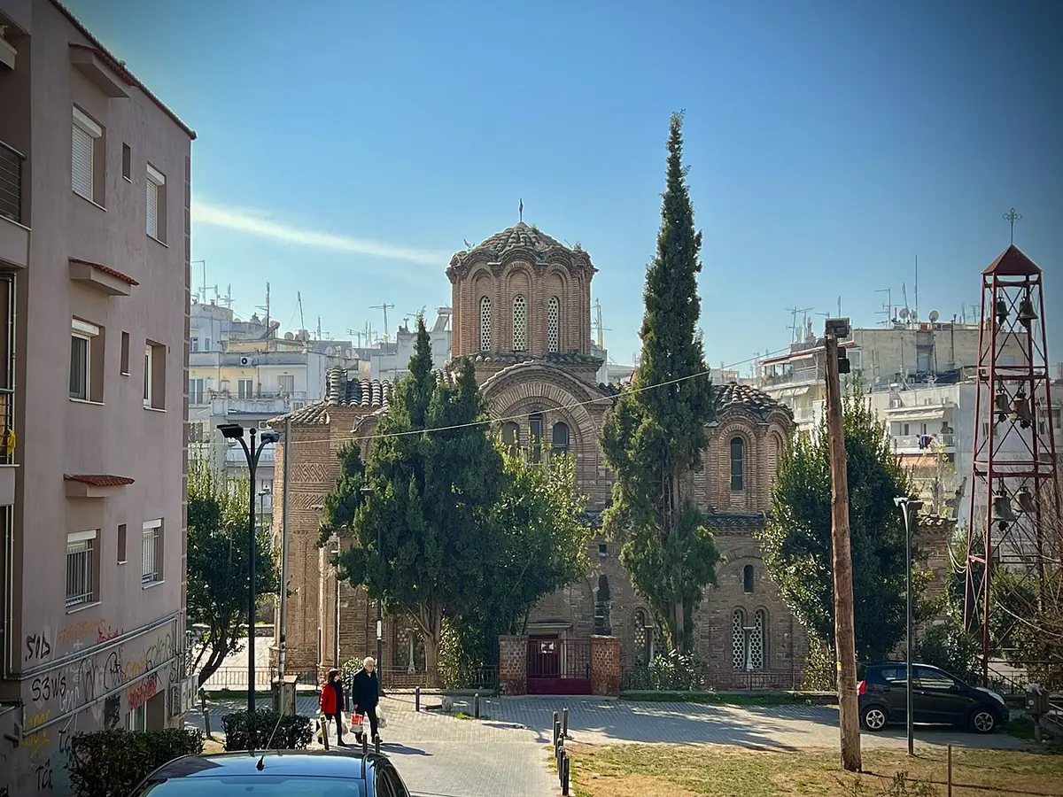 Brick Byzantine church with several small domes among cypress trees and modern apartment buildings in Thessaloniki
