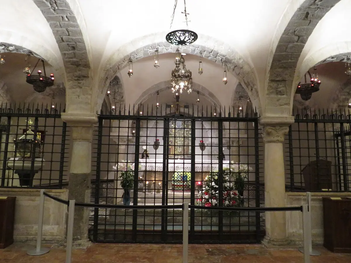 Cripta abovedada de la basílica de Bari, con una reja de hierro delante del altar que se alza sobre las reliquias de San Nicolás, iluminada por lámparas de plata