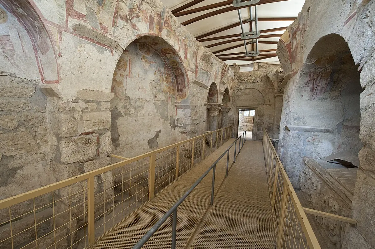 Nave lateral abovedada de la iglesia bizantina de San Nicolás en Demre, con frescos desvaídos en los muros y un sarcófago de mármol junto a una pasarela