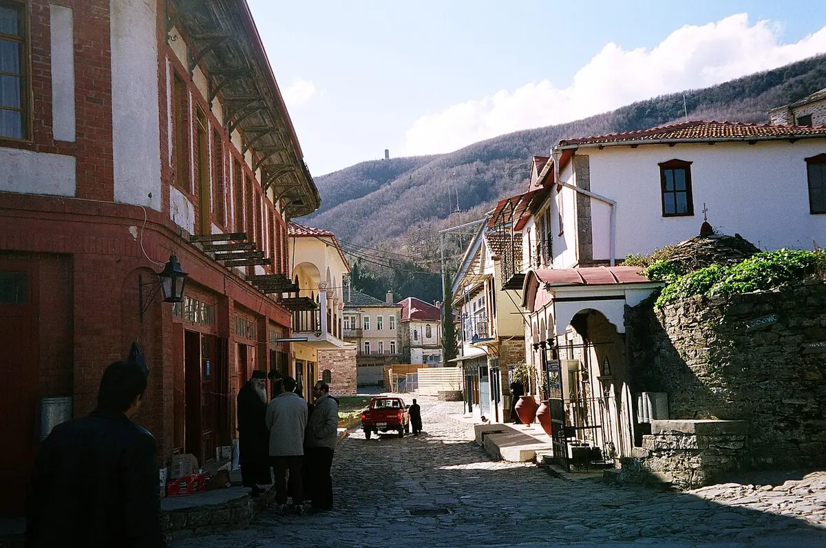 A cobbled street in Karyes on Mount Athos lined with old buildings with wooden balconies, wooded hills behind