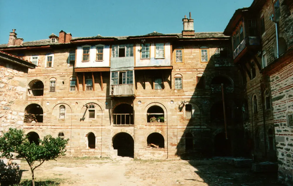 Old stone and timber monastery buildings with wooden balconies and arched openings around a sunny courtyard