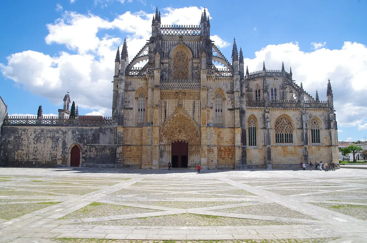 Ornate Gothic stone monastery facade with pinnacles and a large carved doorway across a wide paved square