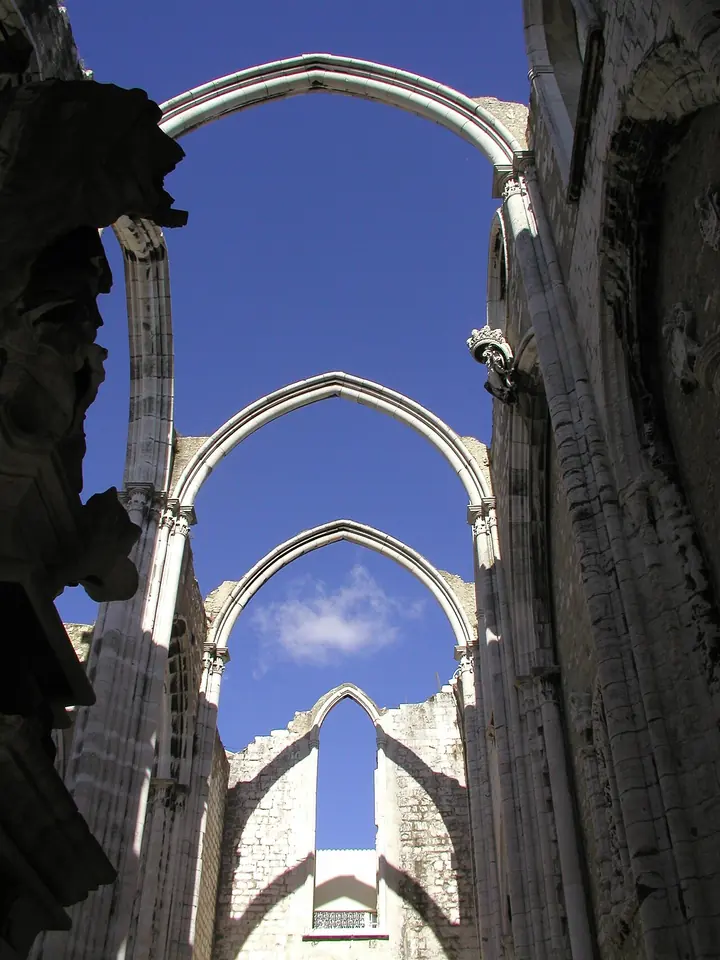 Roofless Gothic church nave with tall pointed stone arches open to a blue sky