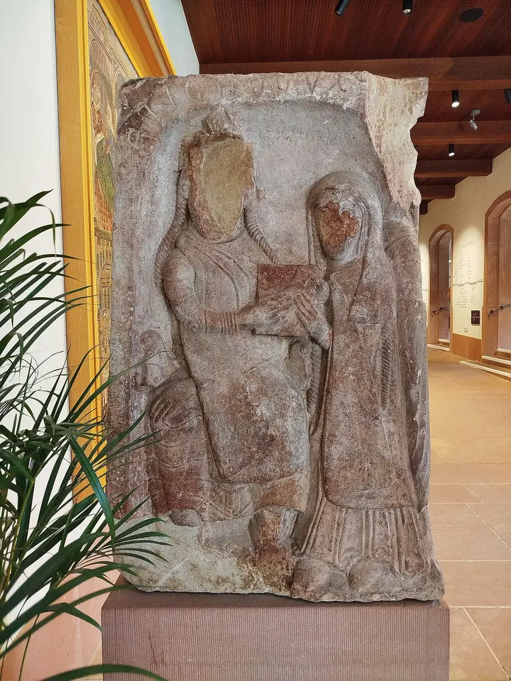 A weathered sandstone relief of a seated nobleman handing a book or charter to a veiled woman