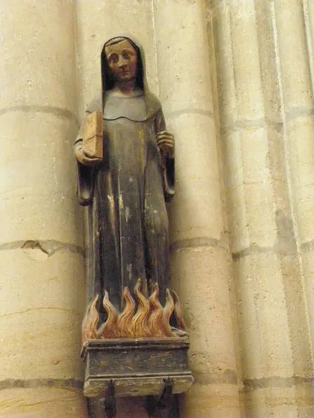 Painted wooden statue of a monk in a dark habit holding a book, standing above carved flames on a stone column