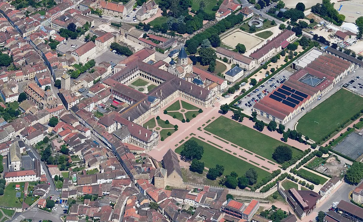 Aerial view of the town of Cluny with the surviving abbey buildings, a long range of monastic wings around green courtyards and gardens among red-roofed houses