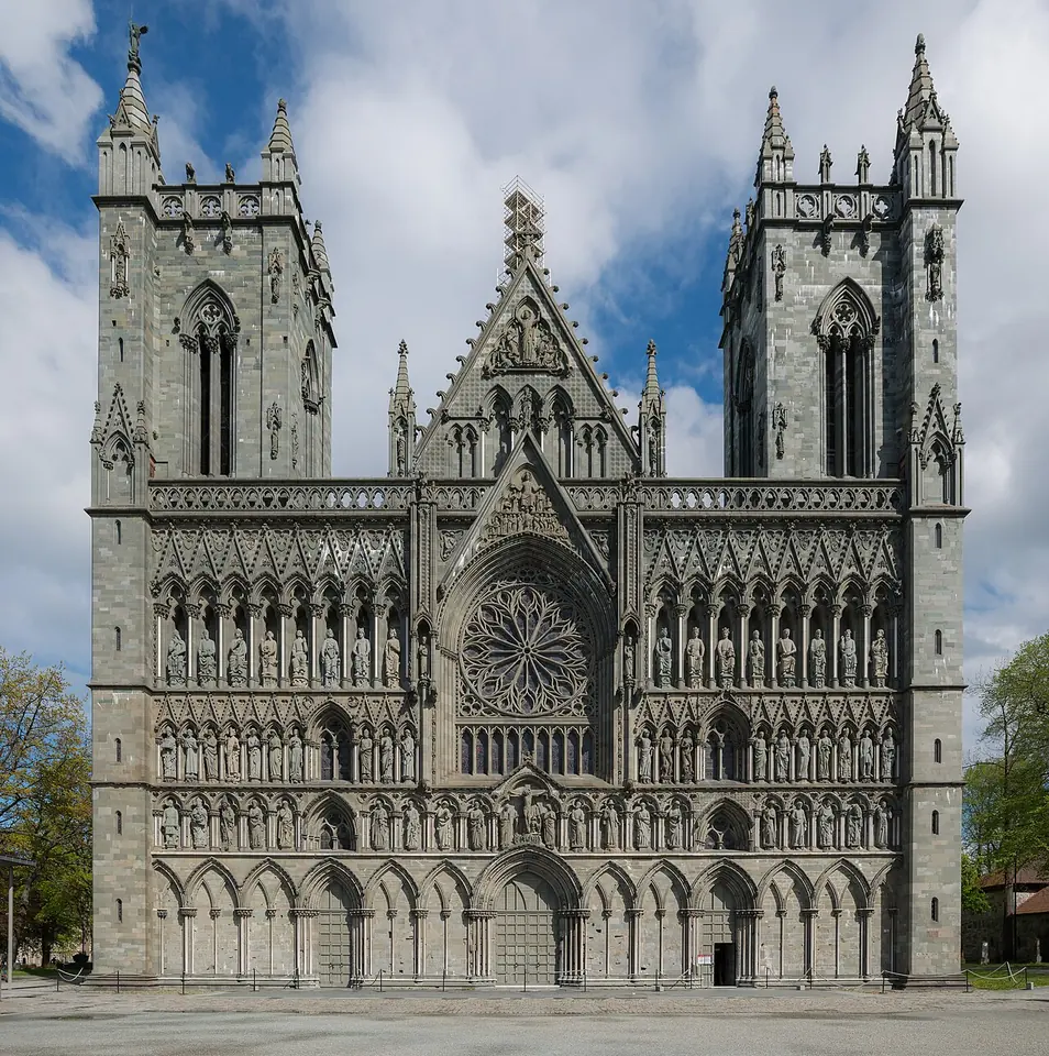 The gray stone west front of Nidaros Cathedral, with two towers, a rose window and rows of statues in niches, under a blue sky