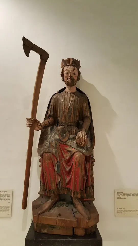 Painted medieval wooden statue of a seated crowned king in a red robe holding a tall long-handled axe