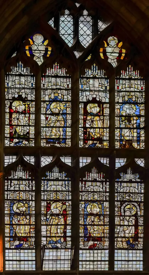 A tall late-medieval stained-glass window with two rows of standing bishop saints in white and gold under canopies