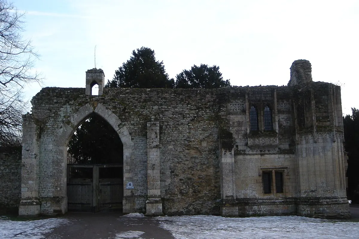 The ruined stone gatehouse of a medieval abbey with a pointed arch and patches of snow on the ground