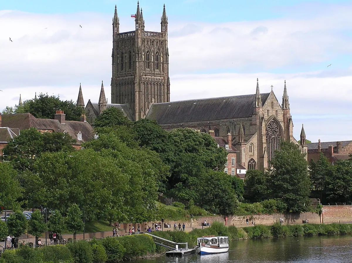 A large Gothic cathedral with a tall square tower rising above trees on the bank of a river
