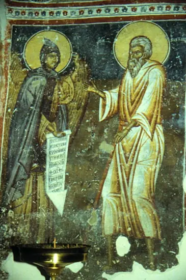 Worn fresco of a winged angel in a dark monastic habit holding an inscribed scroll before a white-robed elderly saint