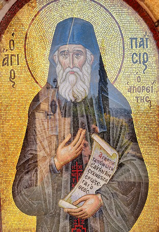 Gold-ground mosaic of St. Paisios as an old monk with a white beard and a blue-black cap, holding an open scroll with Greek writing and raising his hand