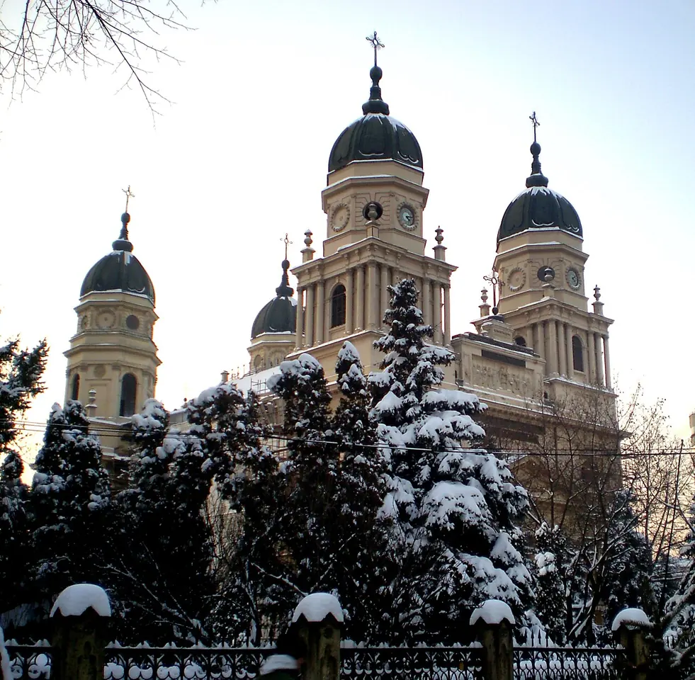 The large cream-colored Metropolitan Cathedral of Iași with four domed towers, seen above snow-covered fir trees