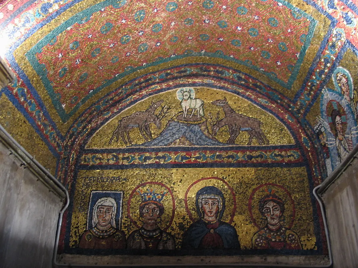 Four mosaic busts of women in a gold field under the Lamb of God on a hill, the first with a square blue halo, in a small vaulted chapel