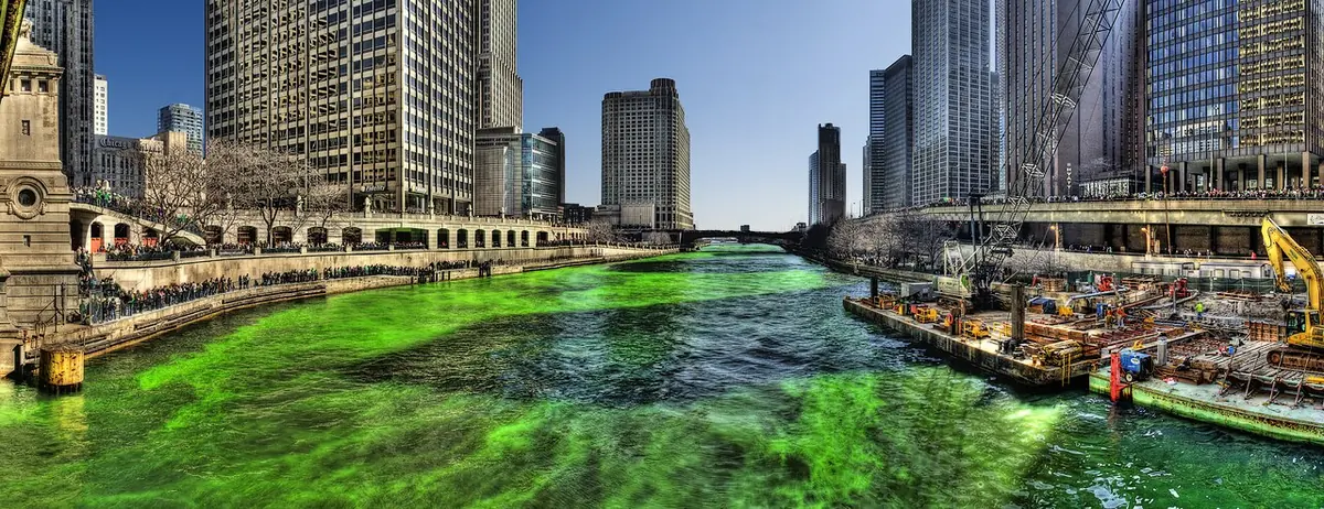 The Chicago River dyed bright green between downtown skyscrapers, seen from the Michigan Avenue bridge