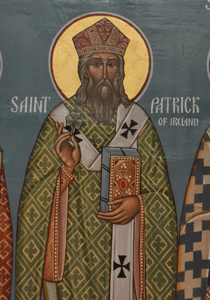 Orthodox icon of St. Patrick with a gold halo and a jeweled miter, in a green patterned robe and white stole with black crosses, blessing with one hand and holding a jeweled Gospel book