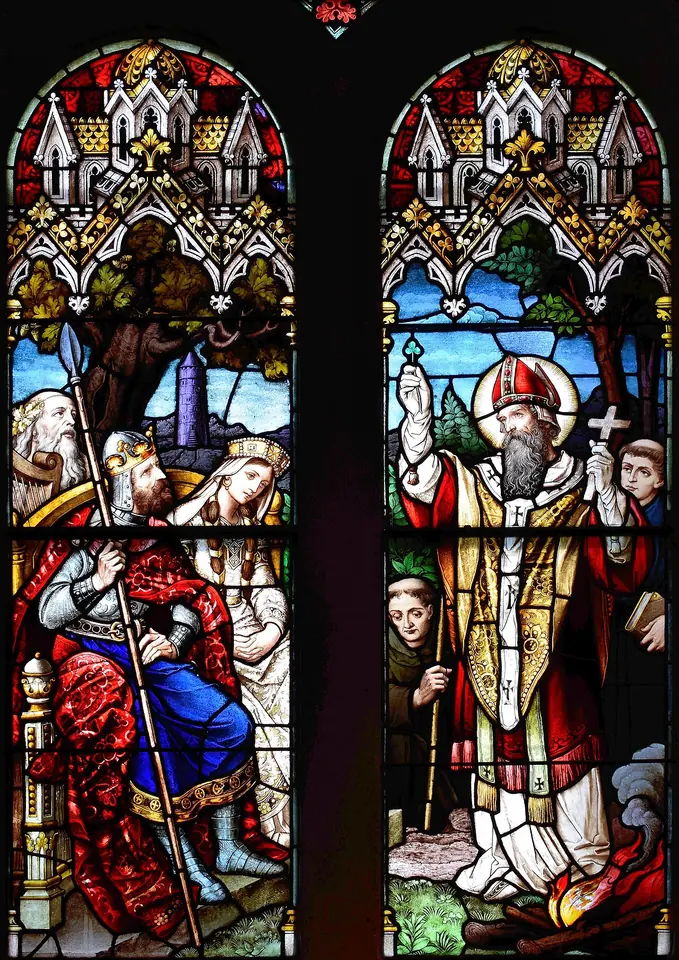 Stained-glass window in two lights showing a crowned king and his court on the left and St. Patrick in a white miter raising his hand and holding a cross on the right, with a fire burning at his feet