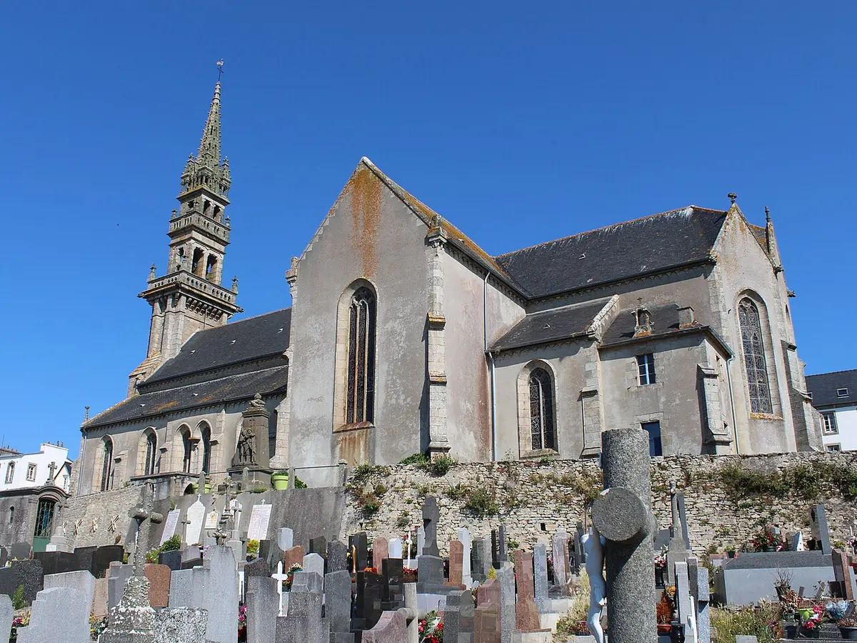 A gray stone church with a tall bell tower and spire above a churchyard of gravestones on the island of Ouessant
