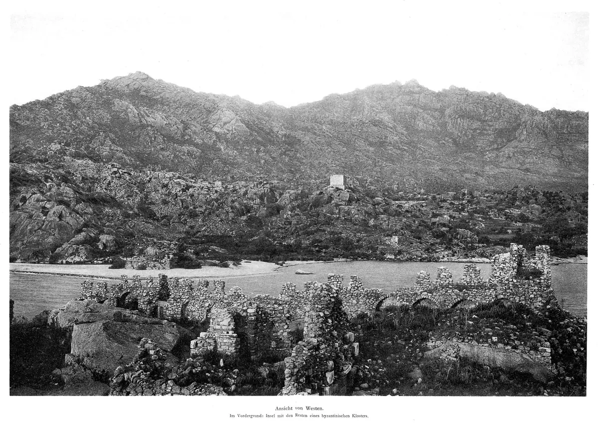 Old black-and-white photograph of the ruins of a Byzantine monastery on a rocky island in the foreground, a lake shore, and a bare, jagged mountain range behind