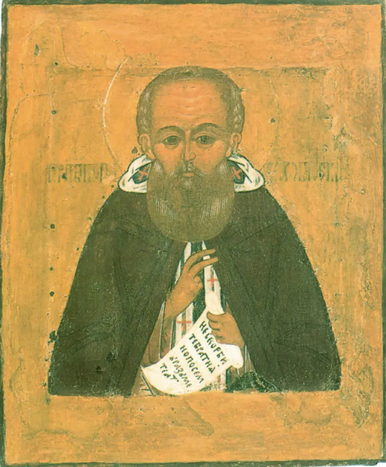 A Russian icon of a bearded monk in a dark green mantle holding an unrolled scroll with writing, on an ochre background